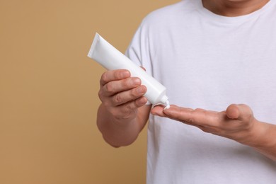 Photo of Man applying body cream onto his hand on light brown background, closeup. Space for text