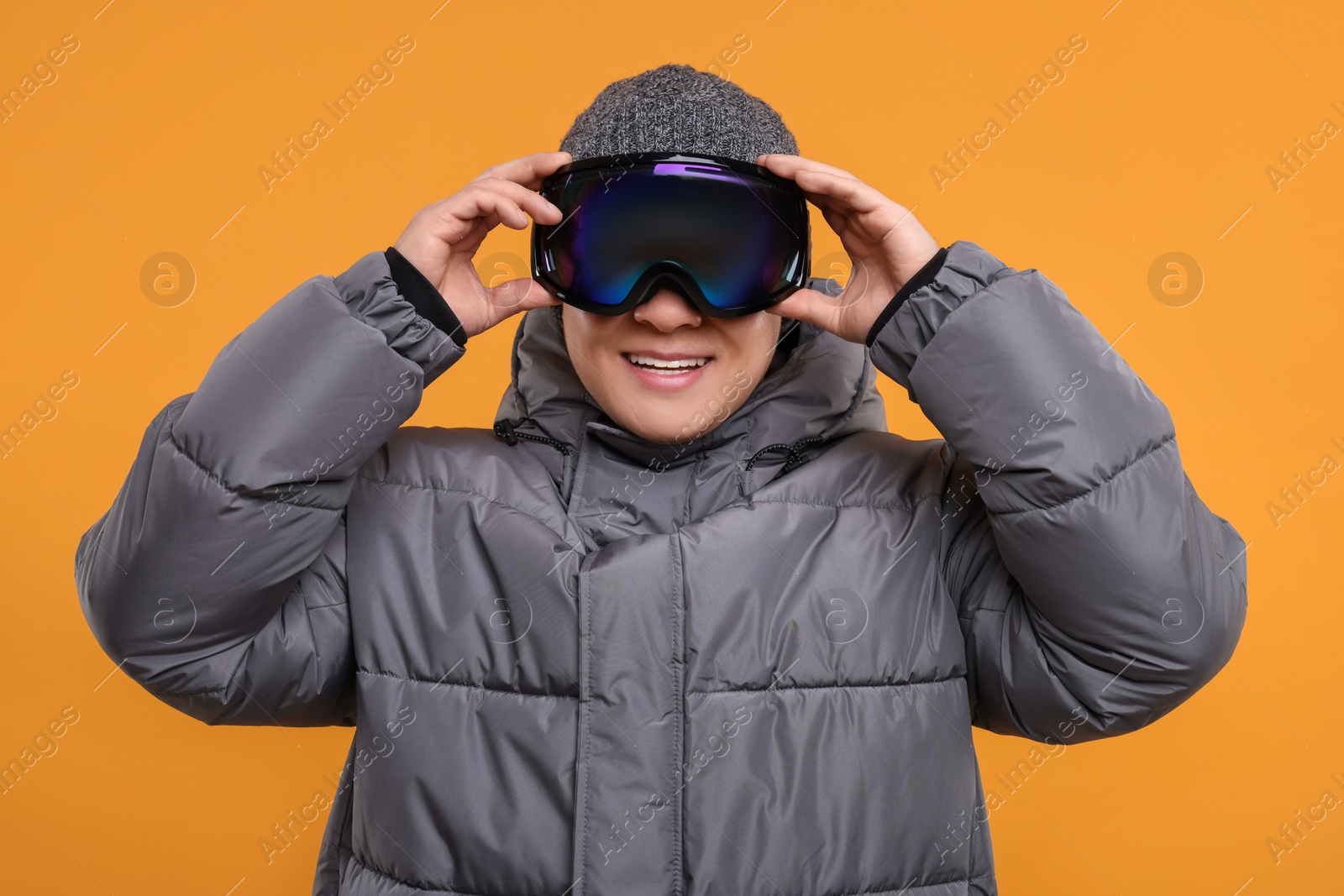 Photo of Winter sports. Happy man in ski goggles on orange background
