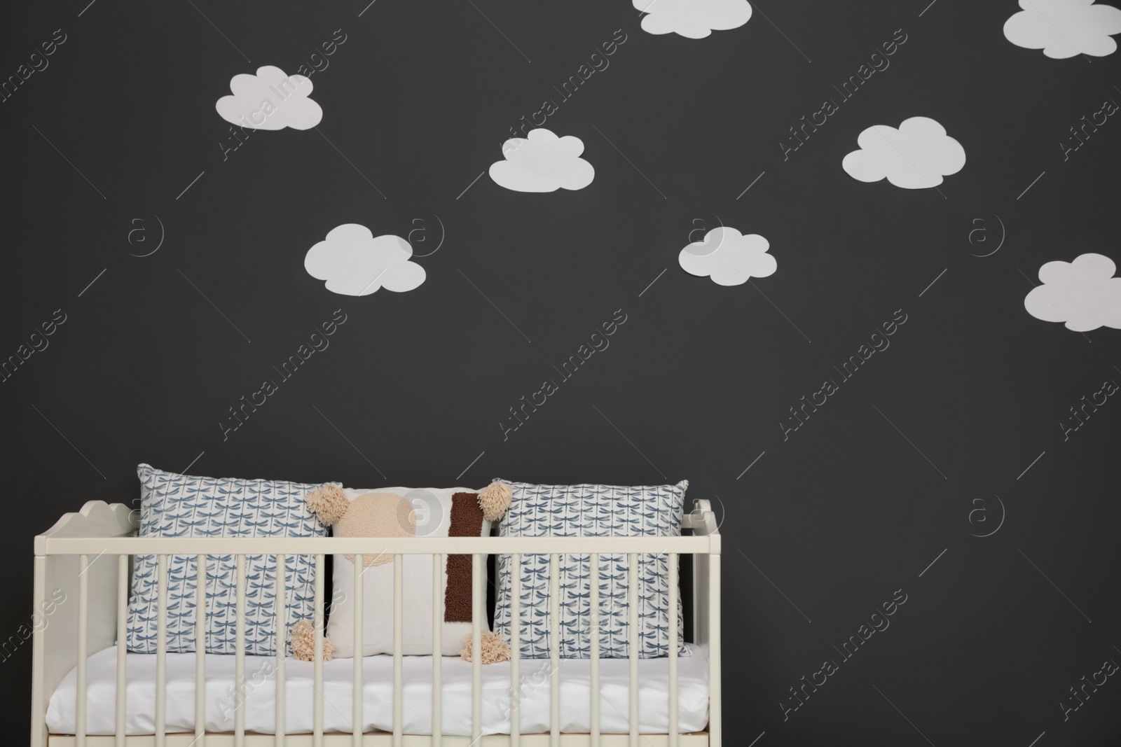 Photo of Cute baby room interior with modern crib near decorative clouds on dark wall