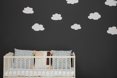 Cute baby room interior with modern crib near decorative clouds on dark wall