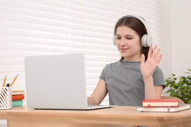 Cute girl using laptop and headphones at desk in room. Home workplace