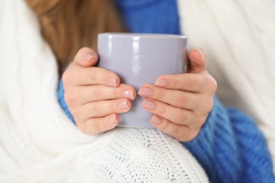 Young woman in cozy warm sweater with cup of hot drink and plaid, closeup