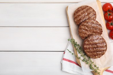 Tasty grilled hamburger patties, cherry tomatoes and thyme on white wooden table, flat lay. Space for text