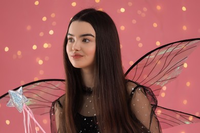 Photo of Beautiful girl in fairy costume with wings and magic wand on pink background