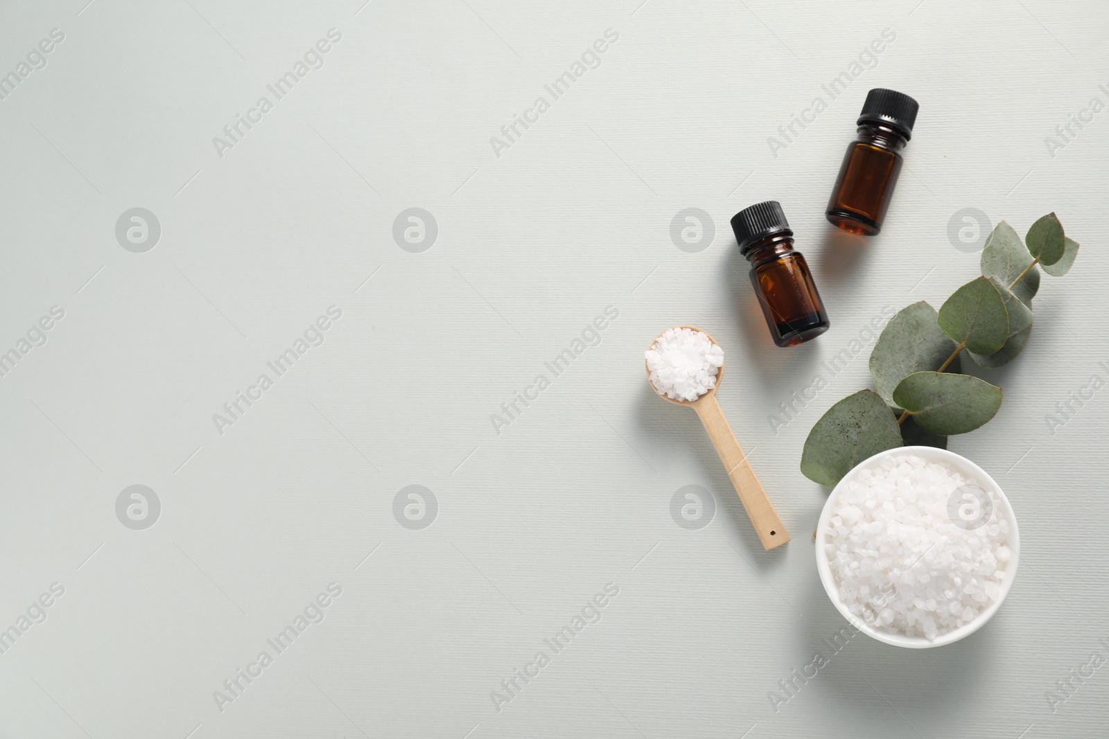 Photo of Aromatherapy products. Bottles of essential oil, sea salt and eucalyptus branch on grey background, flat lay. Space for text