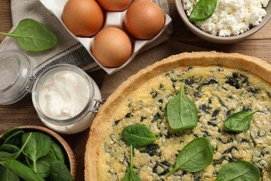 Photo of Delicious homemade spinach pie and fresh ingredients on wooden table, flat lay