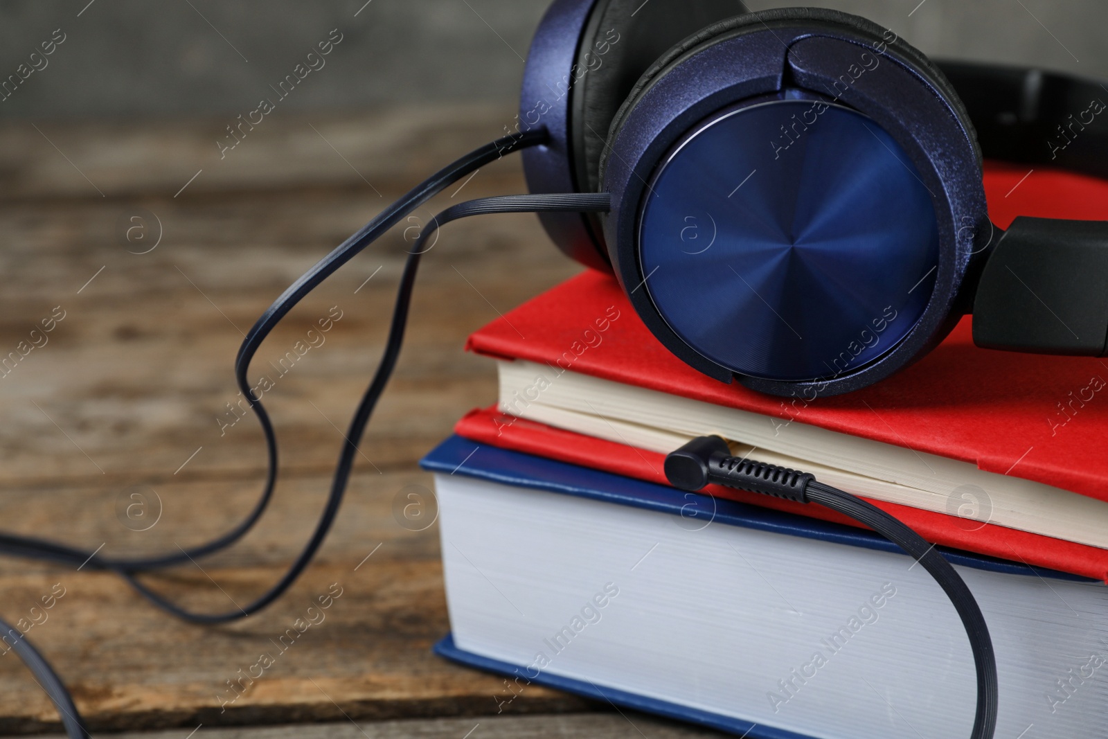 Photo of Modern headphones with hardcover books on wooden table