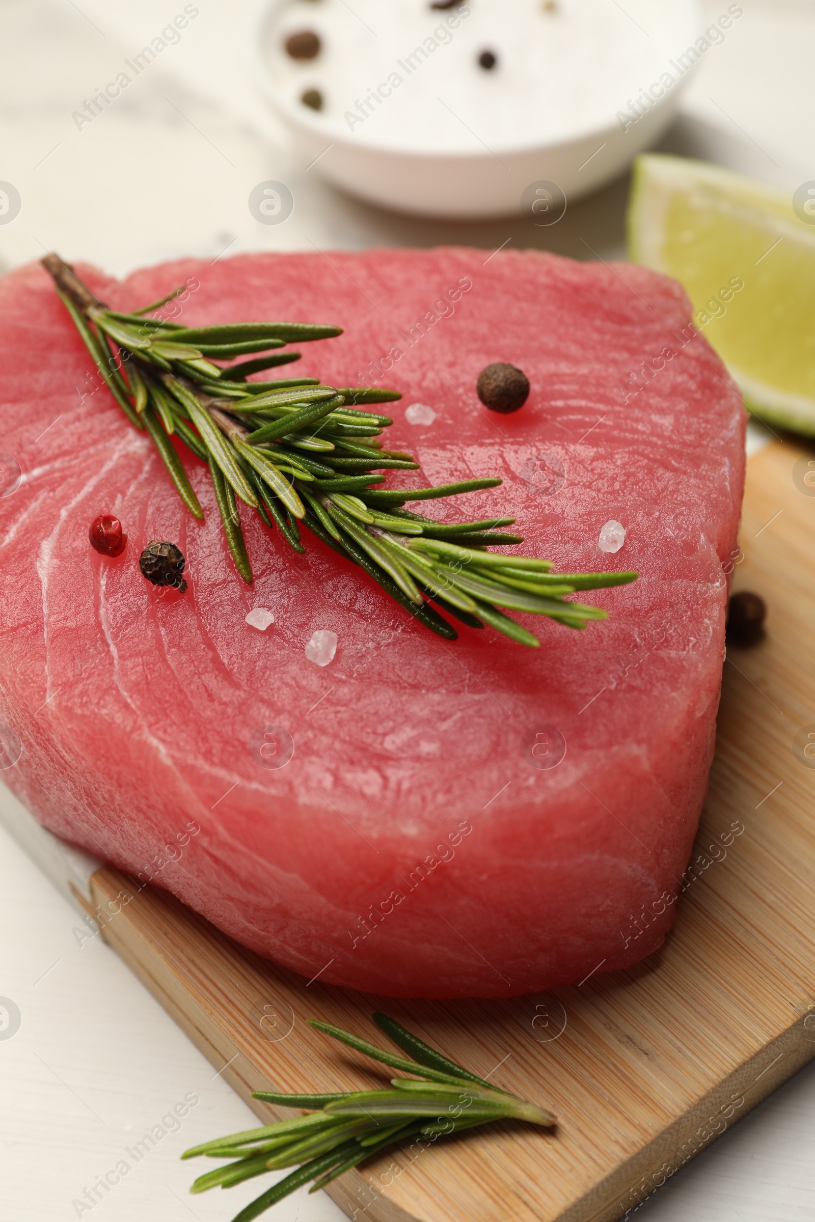 Photo of Raw tuna fillet with rosemary and spices on white table, closeup