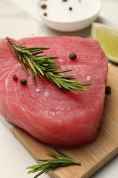 Photo of Raw tuna fillet with rosemary and spices on white table, closeup