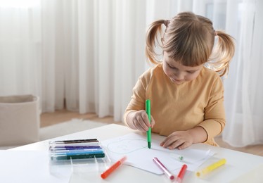 Photo of Cute little girl drawing with marker at white table indoors. Child`s art