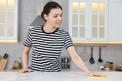 Photo of Woman cleaning countertop with sponge wipe in kitchen
