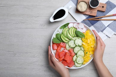 Woman holding delicious poke bowl with salmon and vegetables at wooden table, top view. Space for text