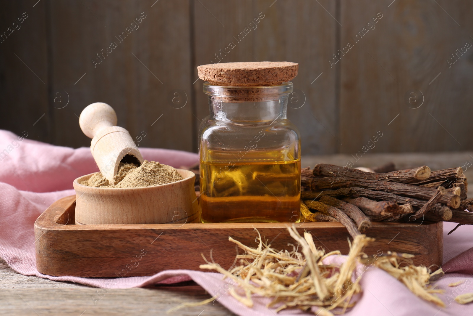Photo of Dried sticks of licorice root, powder and essential oil on wooden table