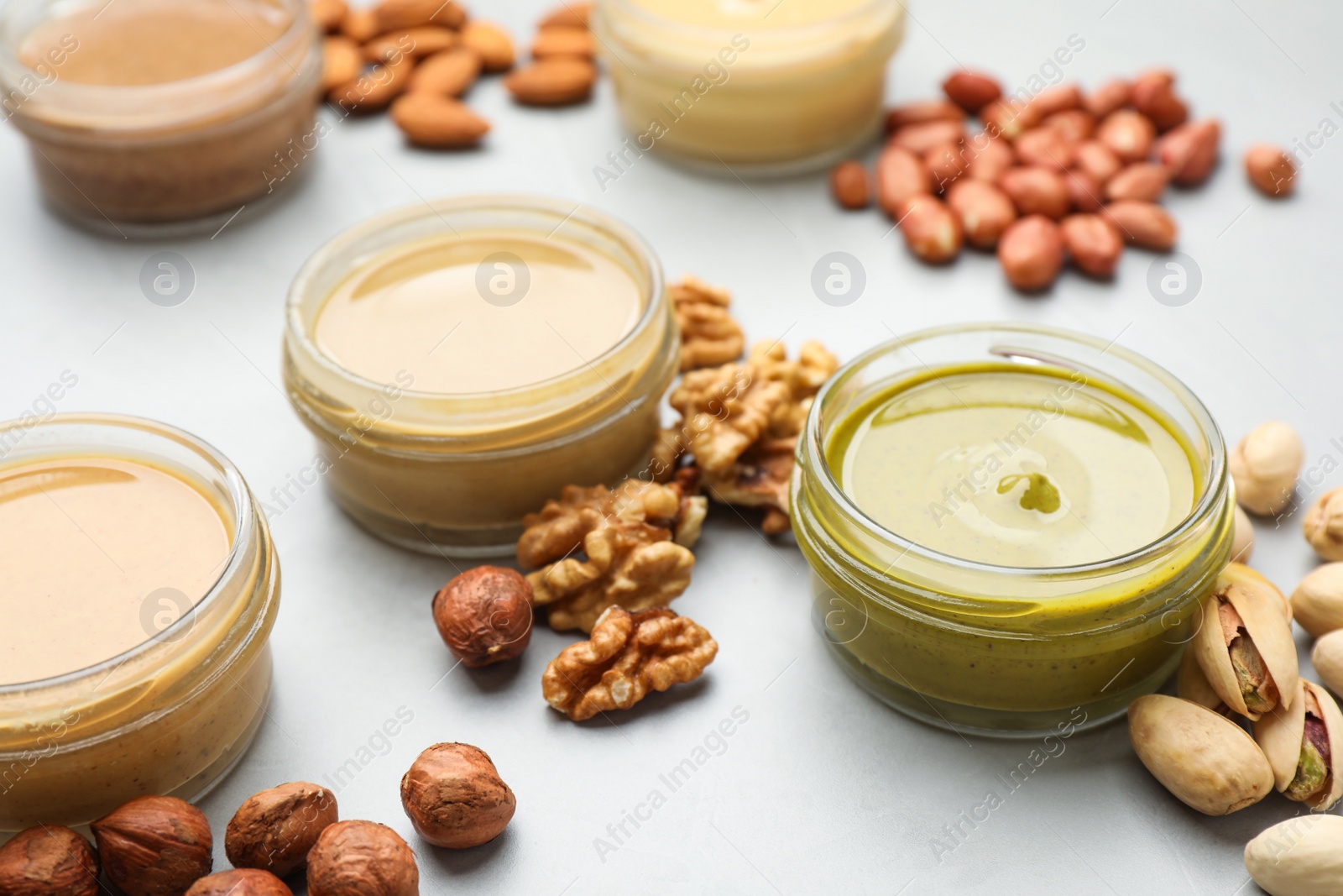 Photo of Different types of delicious nut butters and ingredients on light table, closeup