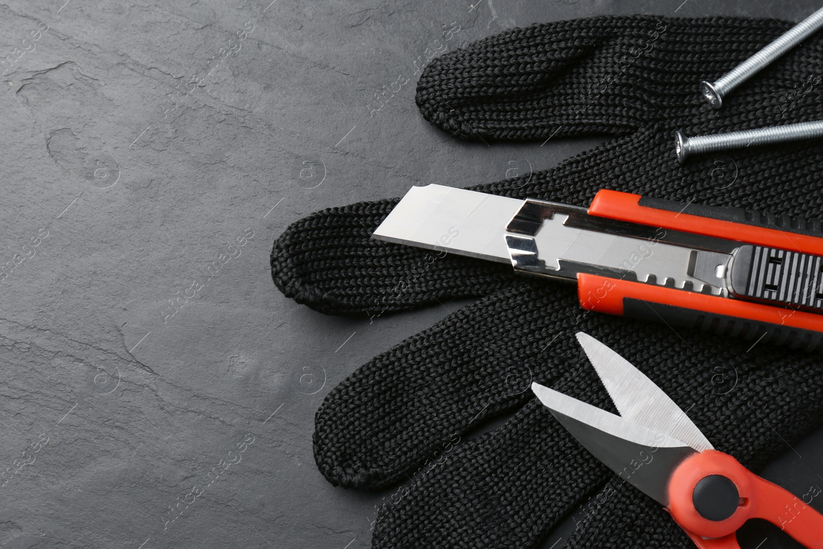 Photo of Glove, utility knife, scissors and screws on black table, flat lay. Space for text