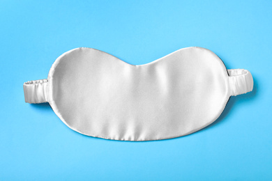 Photo of White sleeping mask on light blue background, top view. Bedtime accessory