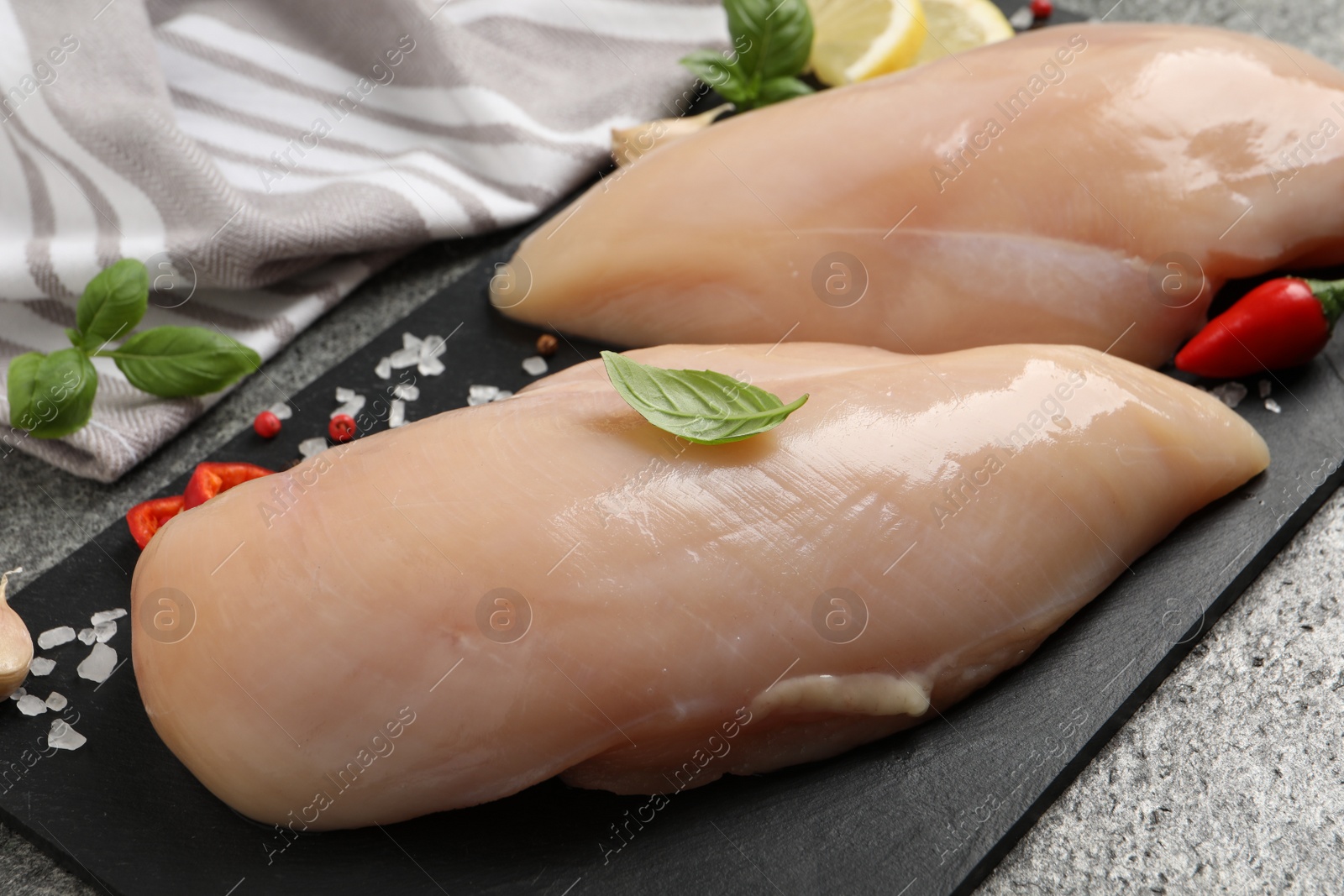 Photo of Raw chicken breasts and ingredients on grey table, closeup