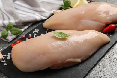 Photo of Raw chicken breasts and ingredients on grey table, closeup