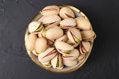 Photo of Tasty pistachios in bowl on black table, top view