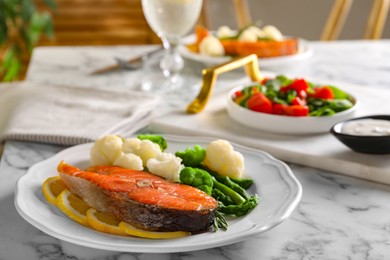 Photo of Healthy meal. Tasty grilled salmon with vegetables and lemon served on white marble table