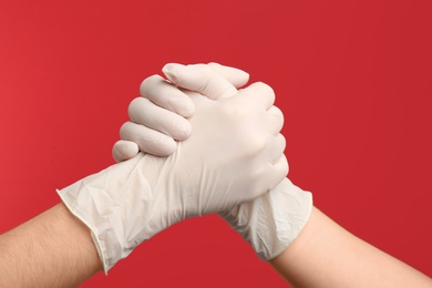 People in medical gloves shaking hands on red background, closeup