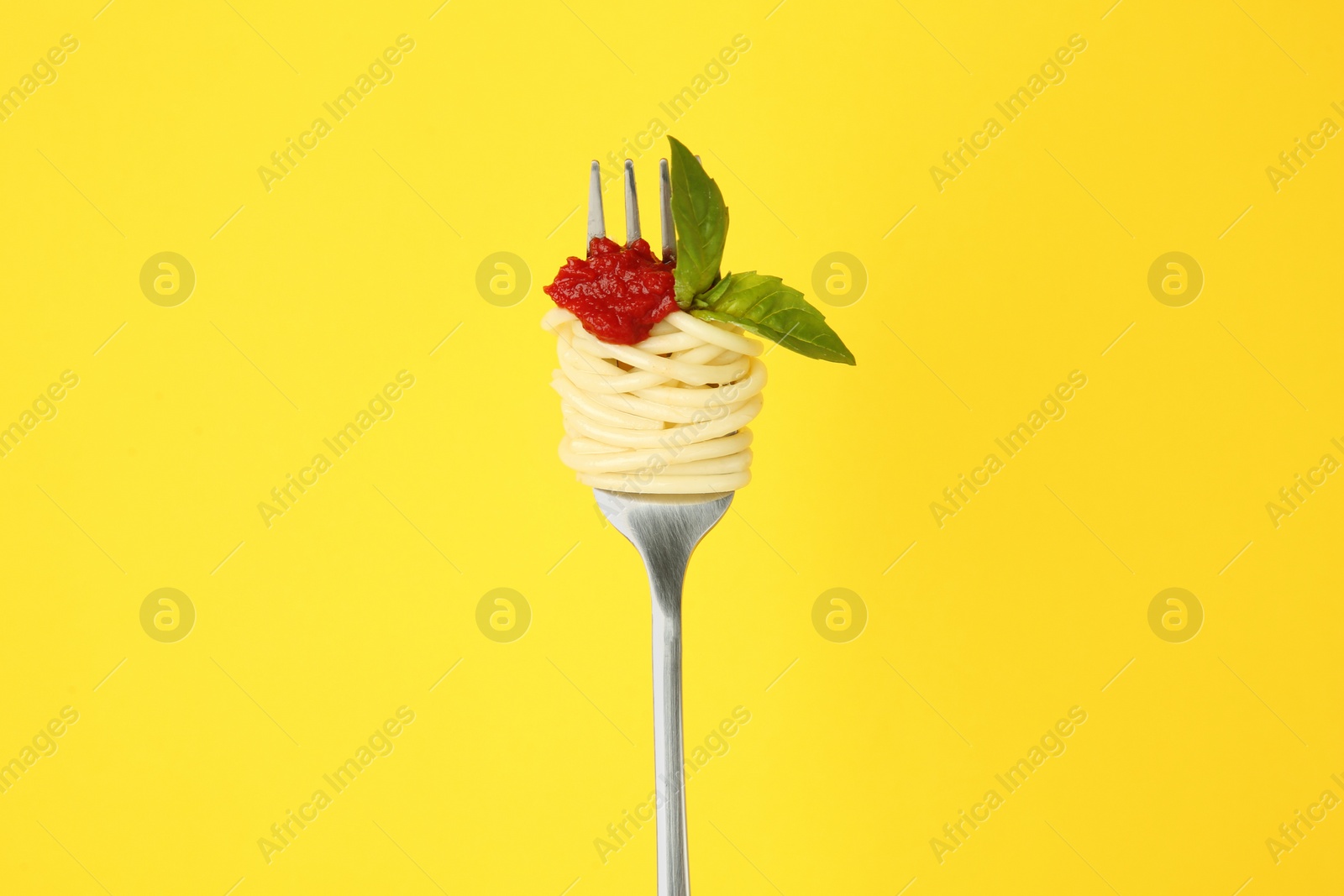 Photo of Fork with tasty pasta, tomato sauce and basil leaves on yellow background