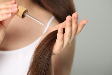 Photo of Woman applying essential oil onto hair on grey background, closeup