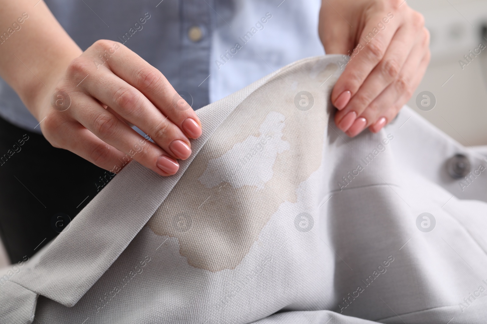 Photo of Woman showing stain from coffee on jacket against blurred background, closeup