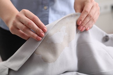 Woman showing stain from coffee on jacket against blurred background, closeup