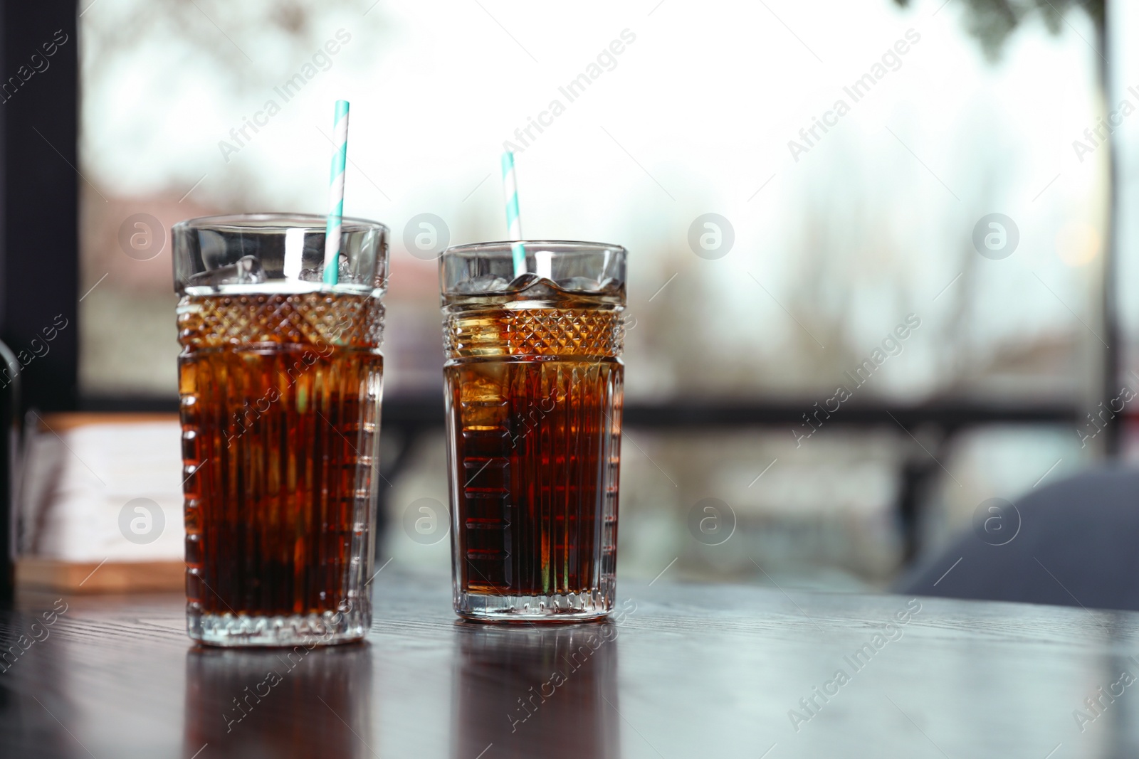 Photo of Glasses with refreshing cola and ice cubes on table indoors. Space for text