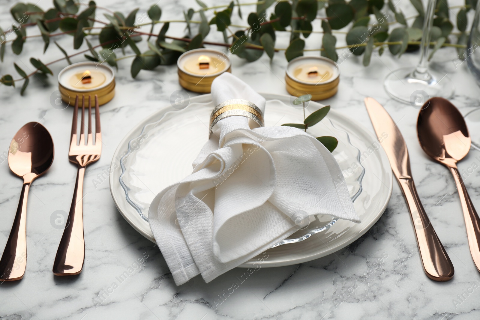 Photo of Beautiful place setting with candles and eucalyptus on white marble table