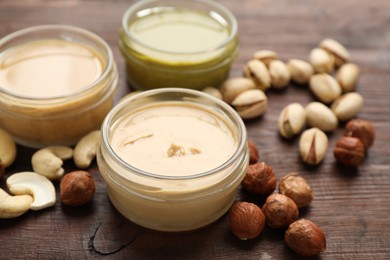 Photo of Different types of delicious nut butters and ingredients on wooden table, closeup