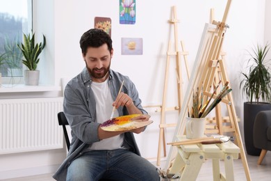 Man painting in studio. Using easel to hold canvas