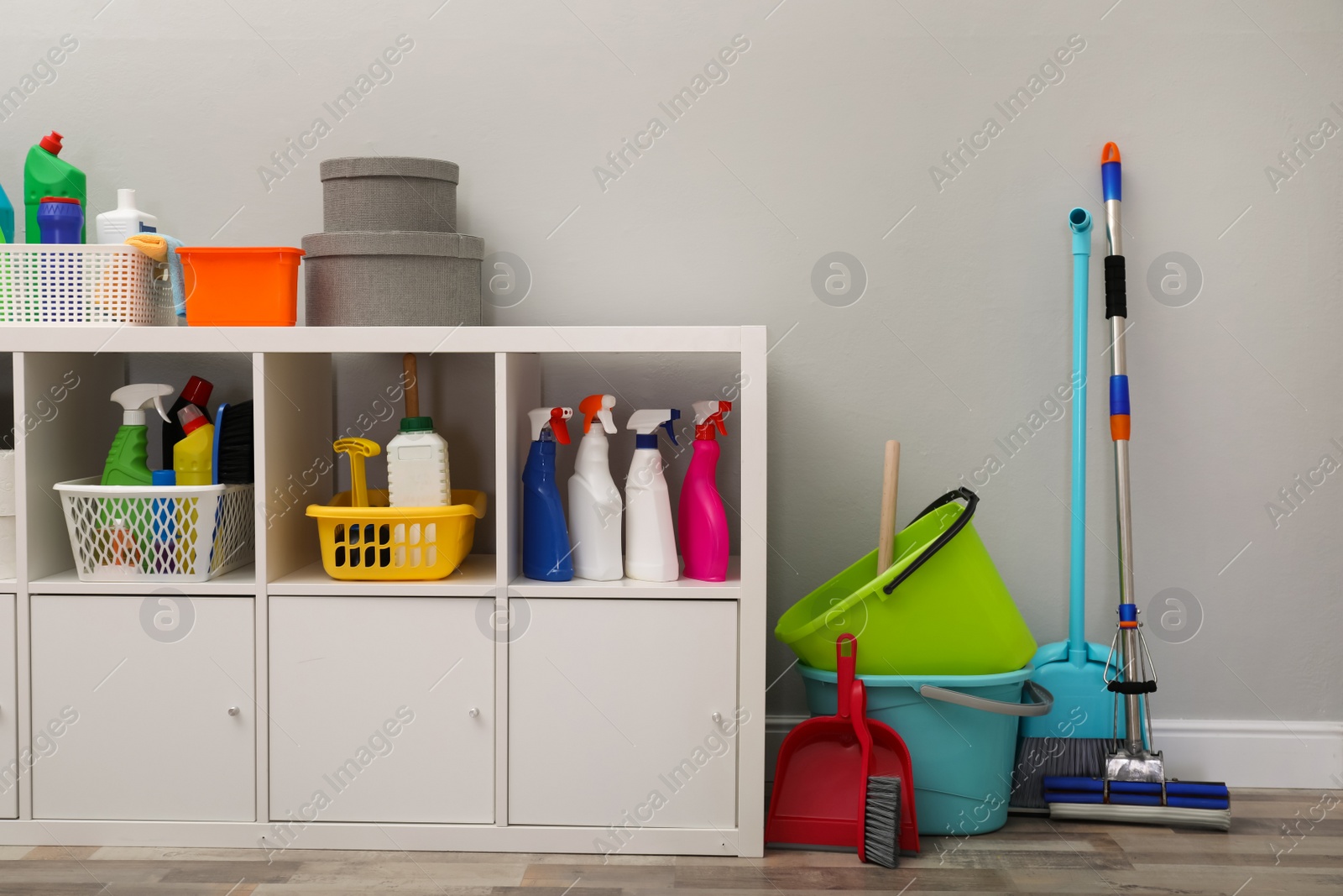 Photo of Shelving unit with detergents and cleaning tools near light grey wall indoors