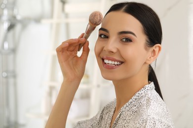 Photo of Beautiful young woman applying face powder with brush in bathroom at home
