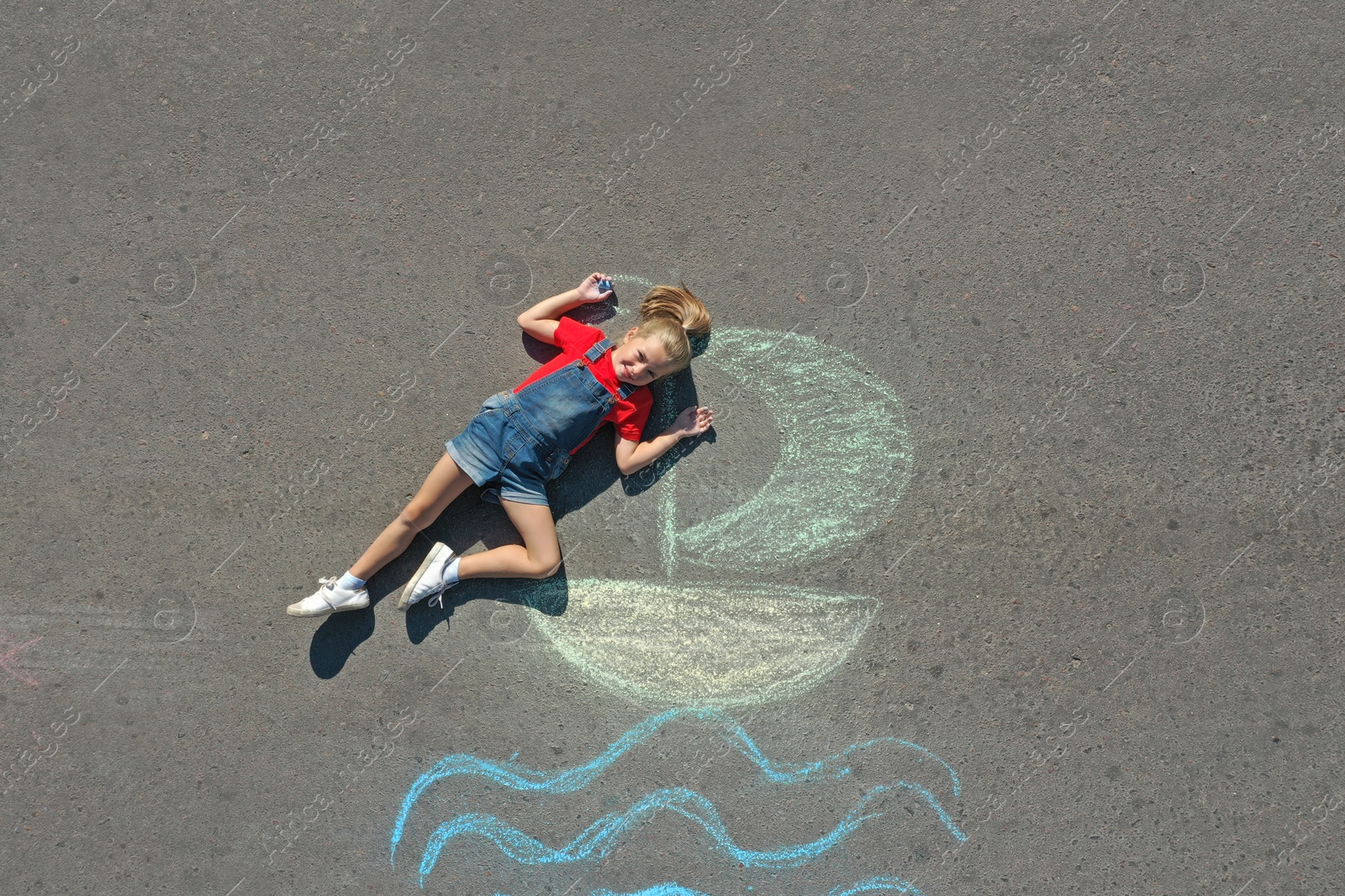 Photo of Cute little child lying near chalk drawing of boat on asphalt, top view