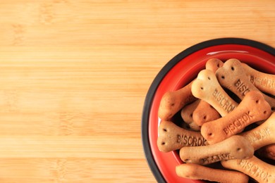 Bone shaped dog cookies in feeding bowl on wooden table, top view. Space for text