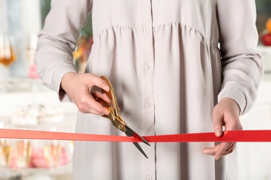 Photo of Woman cutting red ribbon with scissors indoors at ceremonial event