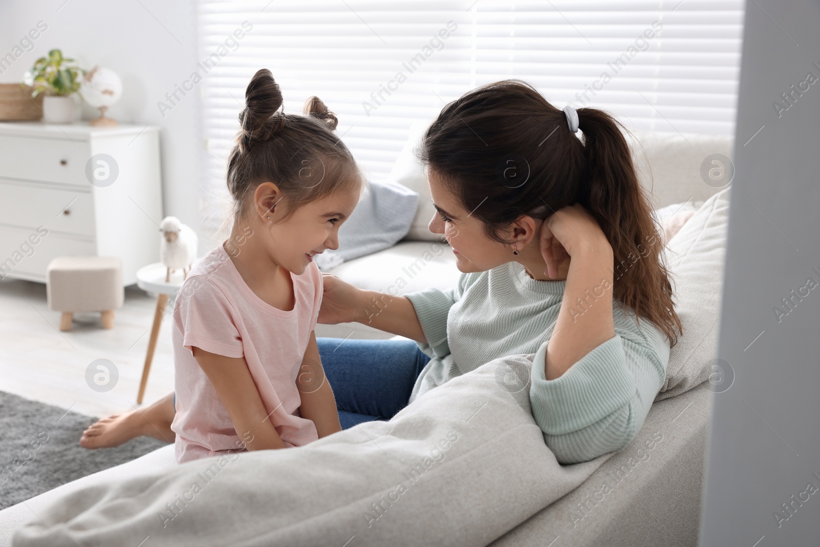 Photo of Young mother and her daughter spending time together on sofa at home