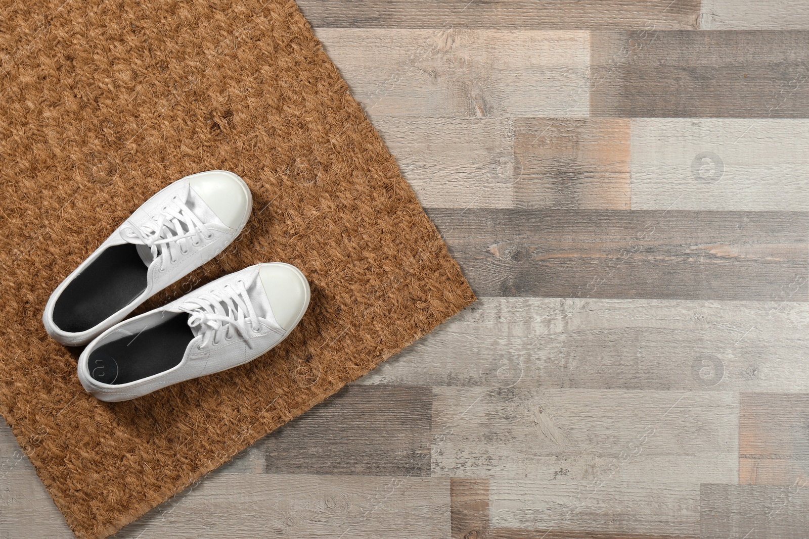 Photo of New clean doormat with shoes on floor, top view. Space for text