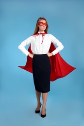 Photo of Confident businesswoman wearing superhero cape and mask on light blue background