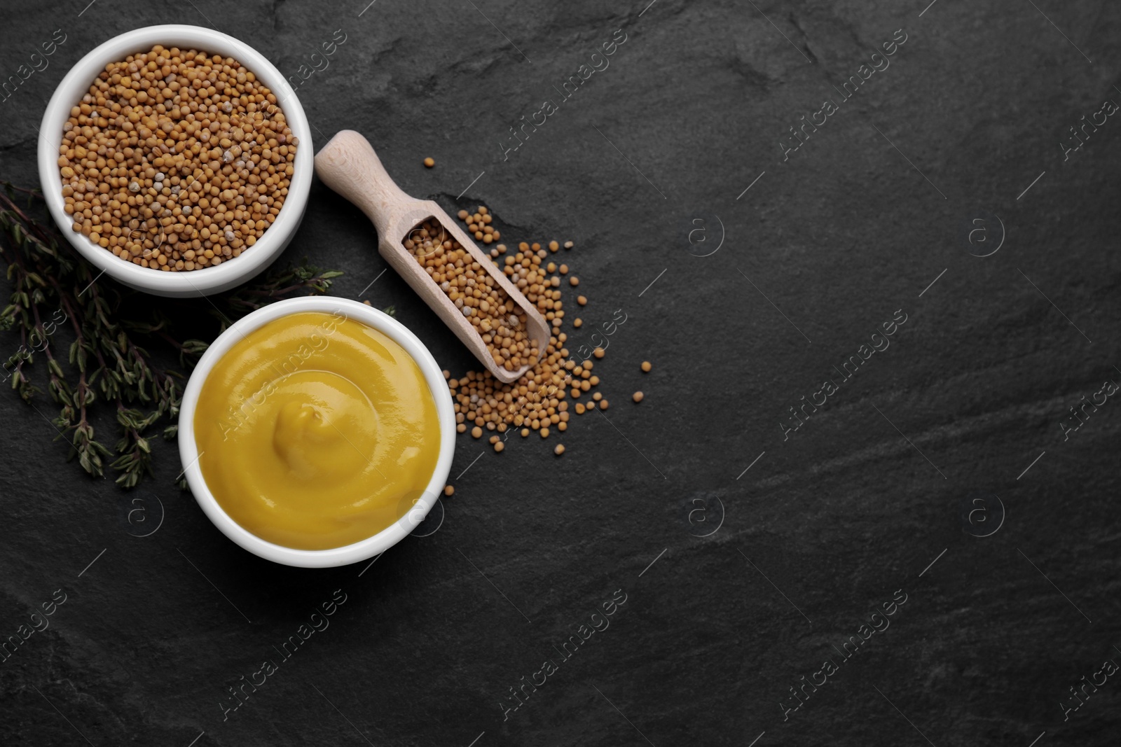 Photo of Delicious mustard, seeds and dry thyme on black textured table, flat lay. Space for text