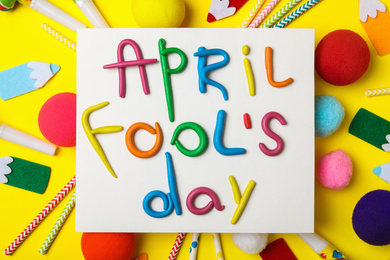 Photo of Paper note with phrase APRIL FOOL'S DAY and decor on yellow background, flat lay