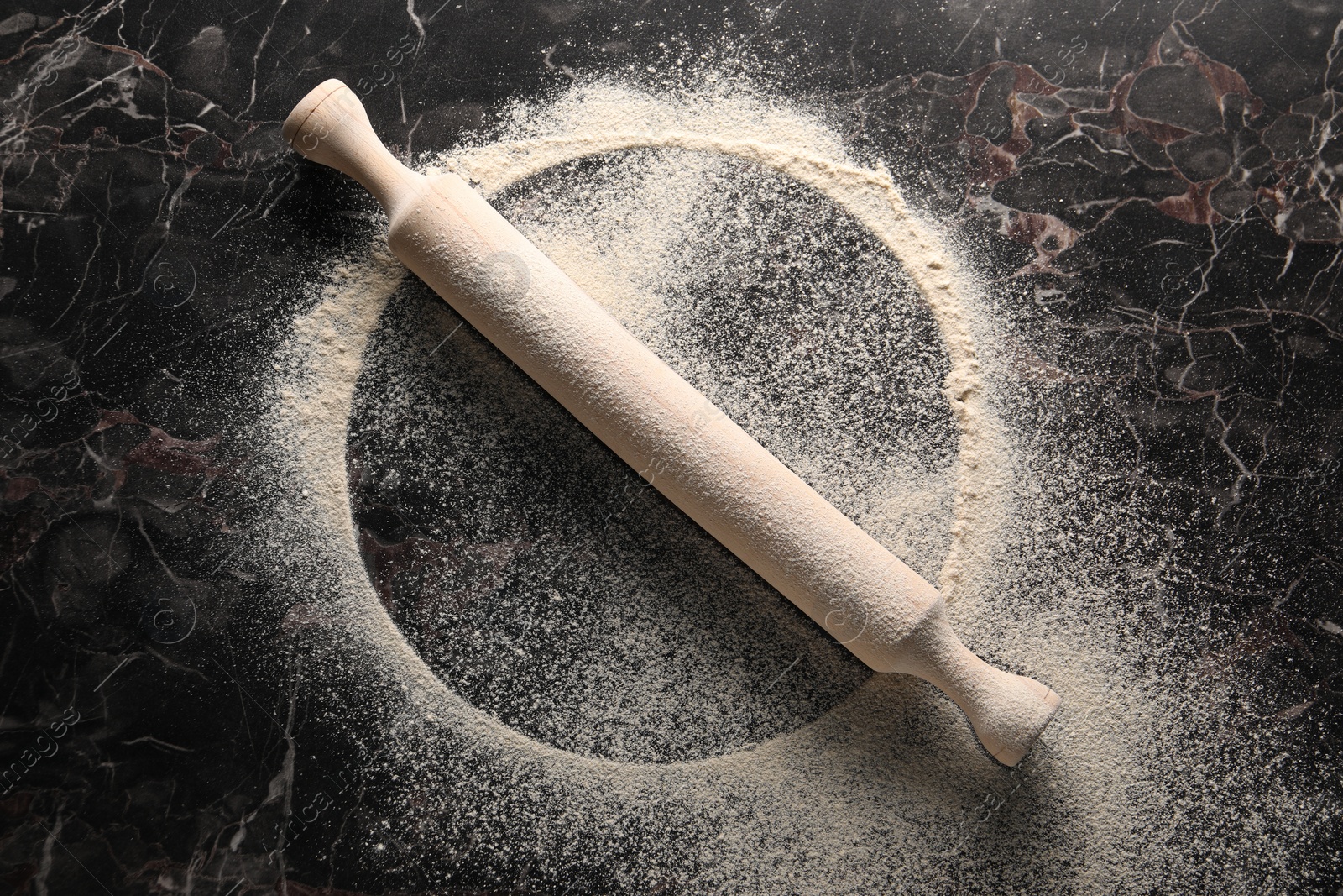 Photo of Imprint of plate on black marble table with flour and rolling pin, top view