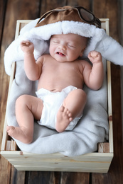 Cute newborn baby wearing aviator hat in wooden crate, above view