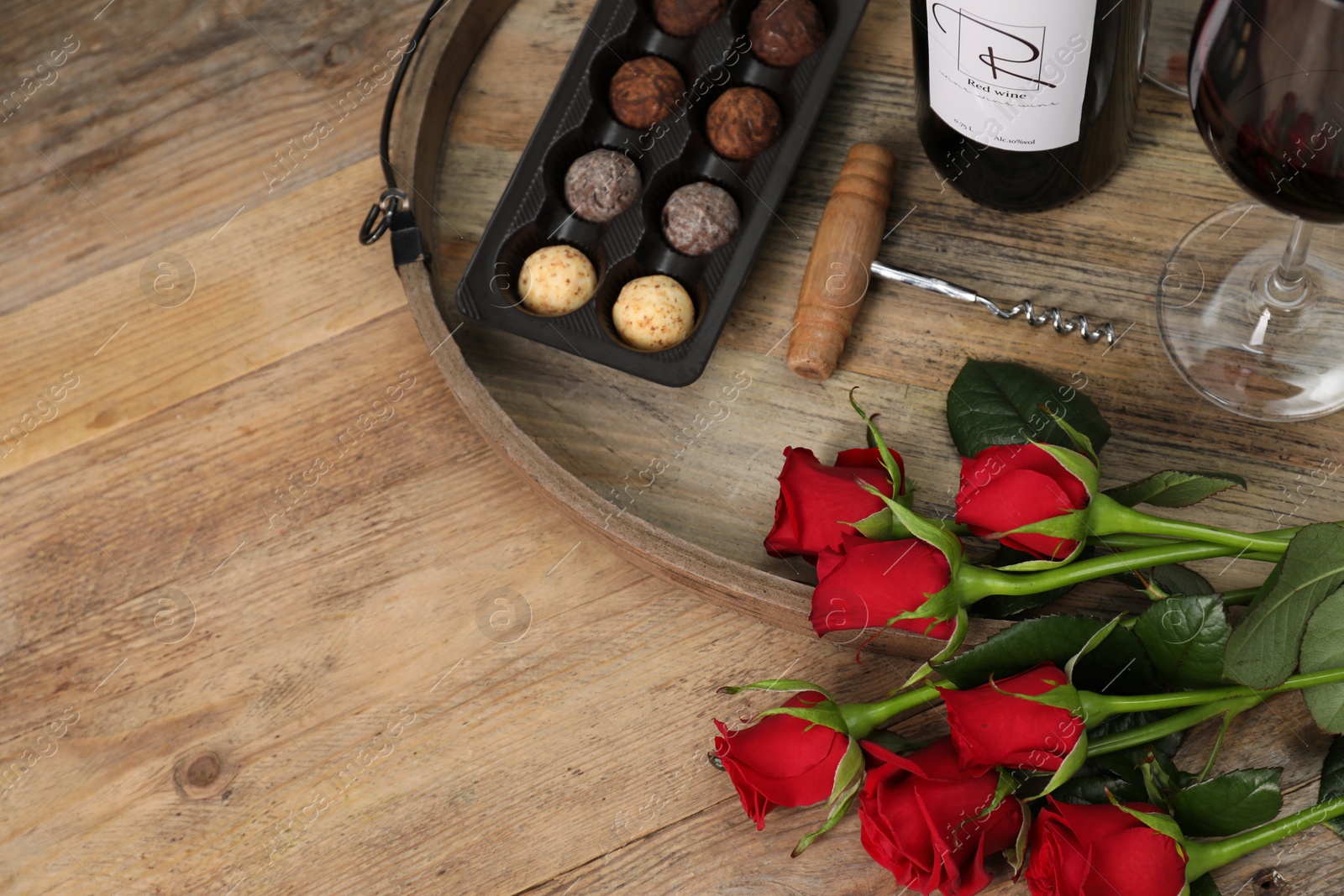 Photo of Red wine, chocolate truffles, corkscrew and roses on wooden table, above view. Space for text