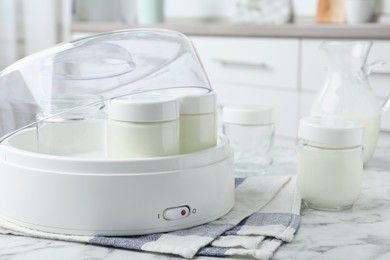 Photo of Modern yogurt maker and jars on white marble table in kitchen