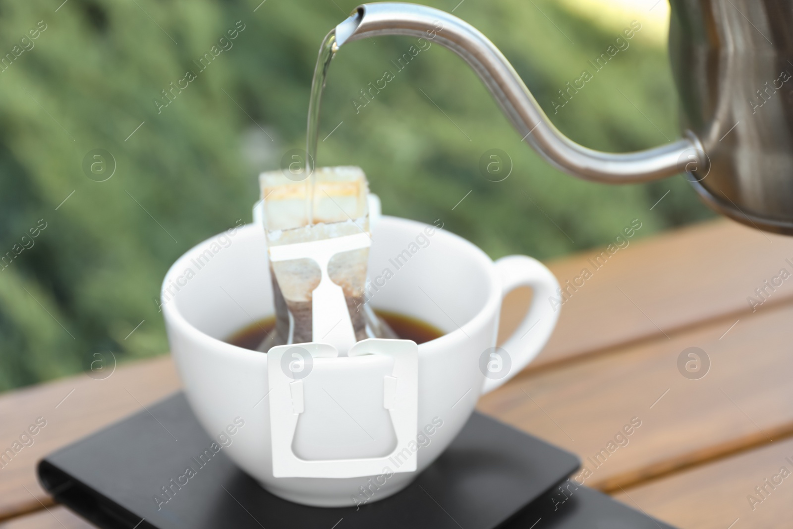 Photo of Pouring hot water into cup with drip coffee bag on wooden table, closeup