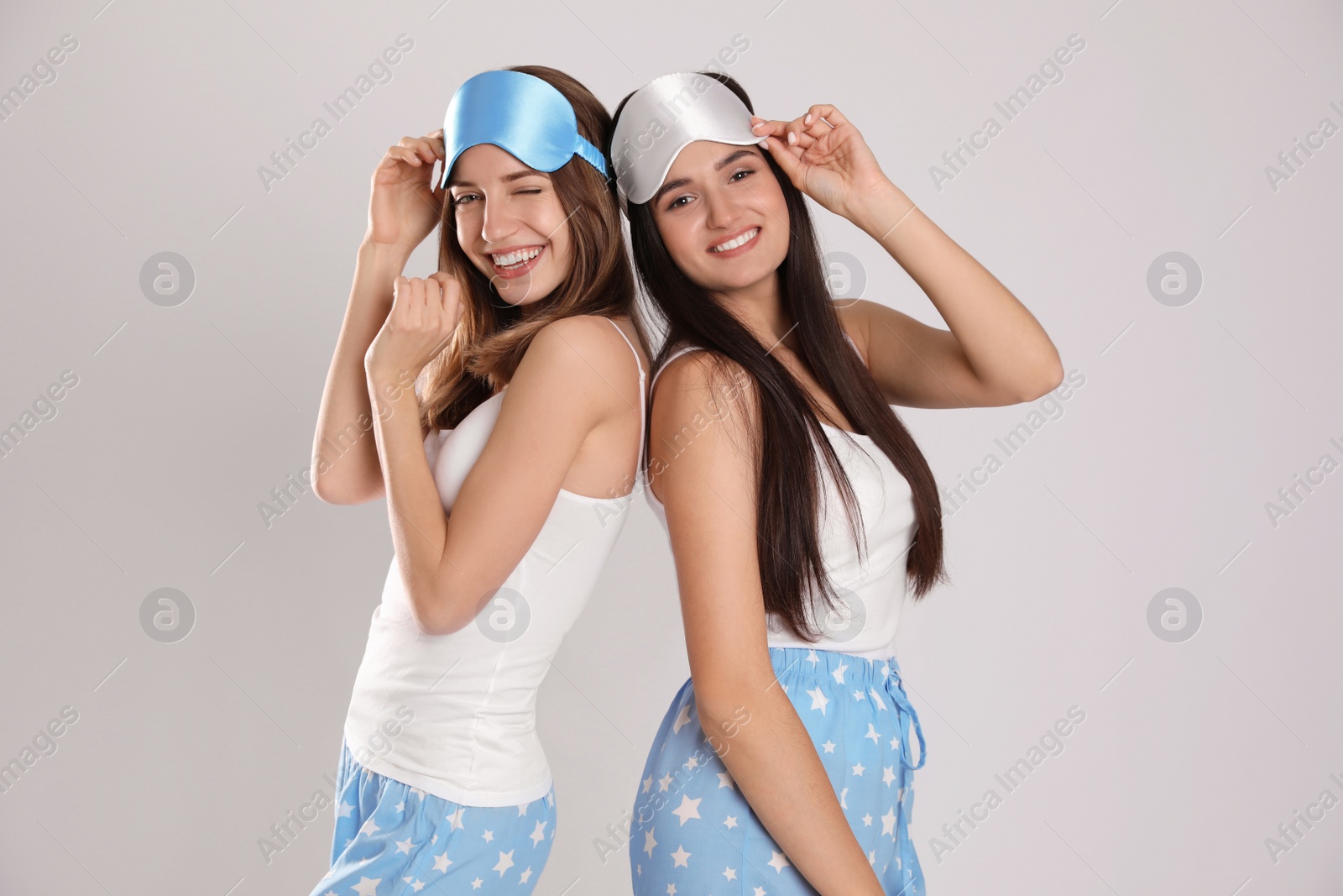 Photo of Beautiful women wearing sleeping masks on light grey background. Bedtime