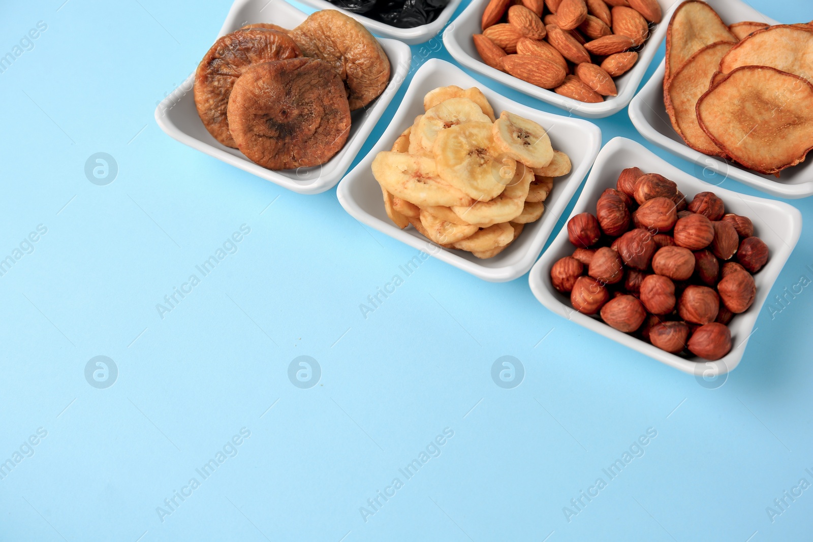 Photo of Bowls with dried fruits and nuts on light blue background, space for text